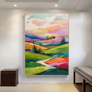 May include: Abstract landscape painting with a vibrant color palette. Rolling hills in shades of green, orange, and purple are under a sky of pink, yellow, and blue. The artwork is framed in a gold-colored frame and hangs on a white wall.