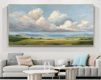 May include: An oil painting of a landscape with a gold frame. The artwork depicts a vast field of green and yellow grass, rolling hills, and a body of water under a cloudy sky. The clouds are white and pink, and the sky is blue.