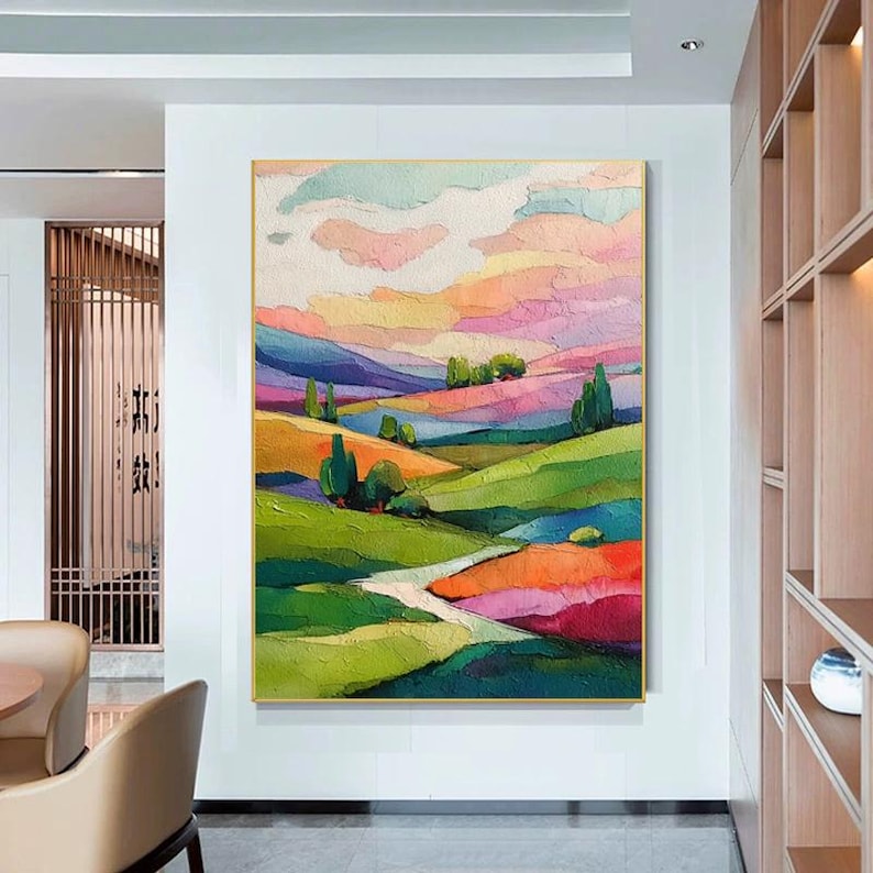 May include: An abstract landscape painting with a gold frame. The artwork features rolling hills in shades of green, orange, and purple, under a sky of pink, yellow, and blue. Trees and a winding path add detail to the colorful scene.