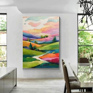 May include: A colorful landscape painting featuring rolling hills and a vibrant sky. The artwork uses a palette of greens, oranges, pinks, and blues to depict a serene countryside scene. The painting is framed and ready to hang.