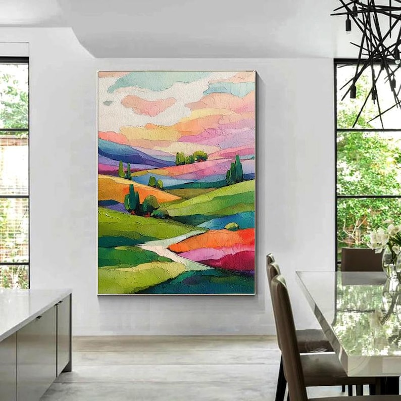 May include: A colorful landscape painting featuring rolling hills and a vibrant sky. The artwork uses a palette of greens, oranges, pinks, and blues to depict a serene countryside scene. The painting is framed and ready to hang.