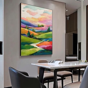 May include: A framed landscape painting with a colorful abstract design. The artwork features rolling green hills, a winding path, and a vibrant sky with pink, orange, and blue hues. The painting is displayed on a gray wall.