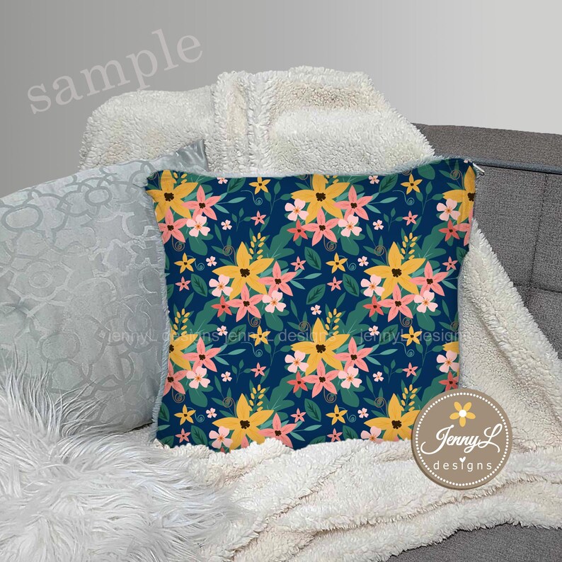 May include: A throw pillow with a floral pattern on a blue background. The pillow features yellow, pink, and green flowers. The pillow is sitting on a white fluffy blanket.