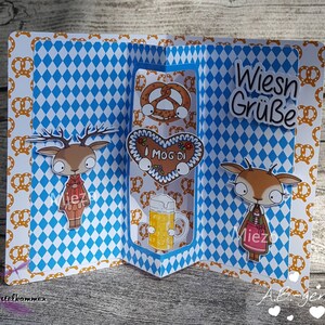 Puede incluir: Una tarjeta a cuadros azules y blancos con un dise&ntilde;o emergente que presenta dos personajes de ciervos, un pretzel, una galleta de jengibre en forma de coraz&oacute;n y una jarra de cerveza. La tarjeta dice "Wiesn Gr&uuml;&szlig;e" e "I mog di".