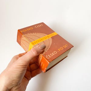 May include: A brown and orange pocket dictionary with the text "POLSKO-ČESKÝ KAPESNÍ SLOVNÍK ČESKO-POLSKÝ" on the cover.