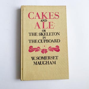 Op de afbeelding: Een vintage boek getiteld "CAKES AND ALE: OR THE SKELETON IN THE CUPBOARD" van W. Somerset Maugham. Het boek heeft een lichtbruine kaft met rode letters en decoratieve bloemelementen. Het boek is in goede staat.