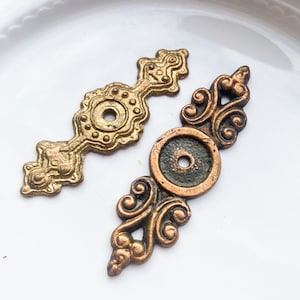 May include: Two ornate metal drawer pulls, one gold and one copper with a green patina. Both have a circular center with a hole for a screw.