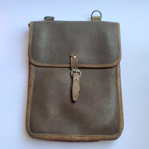 May include: An olive green leather satchel with a flap and buckle closure. The bag has a textured surface and brown trim. It features a shoulder strap attachment and a small buckle. A vintage-style bag.