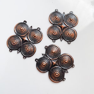 Könnte beinhalten: Drei dekorative Metallornamente mit Kupfer- und Dunkelbronze-Finish. Jedes Ornament hat eine zentrale Sternform mit vier kreisförmigen, spiralförmigen Designs. Die Ornamente haben kleine Schlaufen zum Aufhängen.