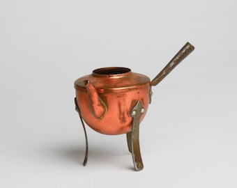 May include: A copper teapot with a handle and three legs. The teapot is made of copper and has a shiny finish.