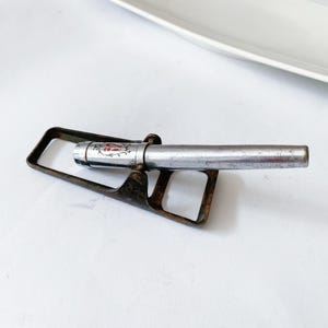 May include: A vintage silver pen rests in a tarnished metal pen holder. The pen's cap features red and silver floral detailing. The pen holder has a rectangular shape with a curved design, and the pen is positioned horizontally.