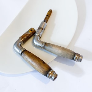 May include: Two antique door handles with wooden grips and metal hardware. The handles are L-shaped, with a silver-colored metal elbow and a wooden grip. The wood has a natural finish, and the metal shows signs of age and wear.