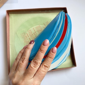 Könnte beinhalten: Eine Sammlung blauer, weißer und roter Schallplattenhüllen in einer braunen Box. Die Hüllen sind aufgefächert und zeigen die Ränder der darin befindlichen Schallplatten. Die Box hat eine hellgrüne Innenseite.