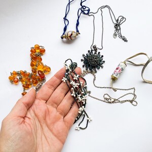 May include: A collection of necklaces featuring various styles and materials, including amber beads, a floral patterned pendant, a blue and white beaded necklace, and a necklace with a star-shaped pendant.
