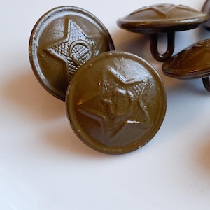May include: Close-up of several olive-green metal buttons. Each button features a raised star emblem with a hammer and sickle design in the center. The buttons have a slightly domed shape and a loop on the back for sewing.