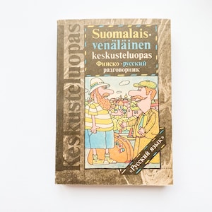 May include: A brown book with the title "Suomalainen-venäläinen keskusteluopas" in Finnish and Russian. The book features a cartoon illustration of two men speaking to each other. The book is titled "Keskusteluopas" on the side.