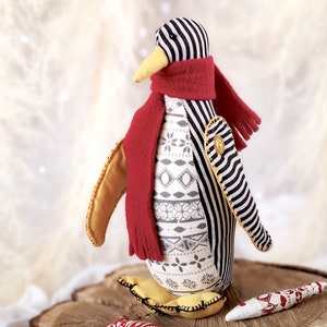 May include: A black and white striped penguin with a red scarf and yellow feet. The penguin is made of fabric and has a white and gray patterned body.