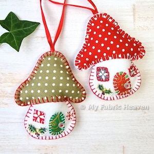 Puede incluir: Dos adornos de champiñón de fieltro hechos a mano con lunares rojos y verdes. Cada champiñón tiene una casita de fieltro blanco con detalles bordados. Los adornos están unidos a una cinta roja.
