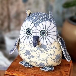 May include: A handmade stuffed owl toy with a blue and white floral pattern. The owl has large white eyes with blue centers and a small, pointed beak.