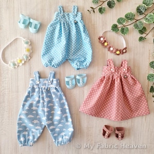 Könnte beinhalten: Eine Sammlung von Puppenkleidung, darunter ein blauer Polka-Dot-Strampler, ein blauer Overall mit Wolkenmuster und ein rosa Polka-Dot-Kleid. Zubehör umfasst Schuhe und Blumenstirnbänder. Puppenoutfits.
