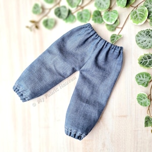 May include: Blue denim pants with white embroidered hearts on the cuffs. The pants are made for a doll or small child.