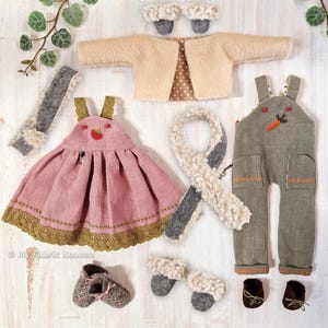 May include: A set of doll clothes for a small doll, including a pink dress with a strawberry design, a green overall with a carrot design, a beige jacket, two pairs of brown shoes, two pairs of grey shoes, and two scarves.
