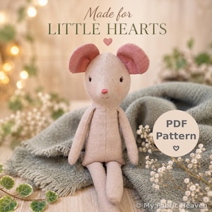 May include: A handmade, light pink mouse doll with large pink ears, black eyes, and a pink nose. The doll is sitting on a gray blanket. The text "Made for LITTLE HEARTS" is at the top, and "PDF Pattern" is in a circle on the right.