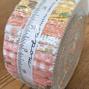 May include: A jelly roll fabric bundle featuring assorted strips in shades of yellow, orange, and white with floral and gingham patterns. A white paper band labeled moda fabrics + supplies wraps the roll, showing a 4-inch measurement scale.