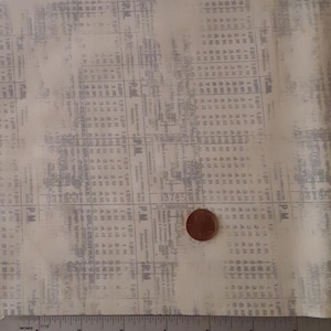 May include: A close-up of a white fabric with a subtle gray print of a newspaper page. The fabric has a textured surface and a vintage look. A ruler is visible at the bottom of the image.