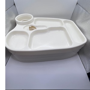 May include: A white plastic divided serving tray featuring a circular cup holder, a central utensil slot, and four distinct rectangular compartments of varying sizes for organizing food items. The tray has a smooth, glossy finish.