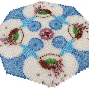 Pode incluir: Um tapete redondo de contas brancas com um desenho floral azul e branco. O tapete é redondo e tem uma borda festonada.