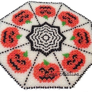 May include: A white beaded table runner with a black and white spiderweb design in the center. The runner is surrounded by eight orange beaded pumpkins with black jack-o'-lantern faces. The text "Linea Creativa" is in the lower right corner.