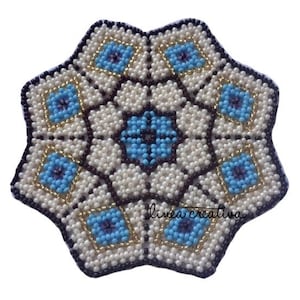 Pode incluir: Um descanso de copo de contas brancas, marrons, azuis e douradas com um design de estrela. O descanso de copo é feito de contas pequenas e tem um padrão geométrico.