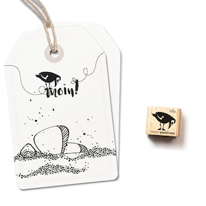 Könnte beinhalten: Ein weißer Geschenkanhänger mit einer schwarz-weißen Illustration eines Vogels und dem Wort "moin!" Ein kleiner Holz-Stempel mit einer schwarz-weißen Illustration eines Vogels und dem Text "ulla cation appletrees" ist ebenfalls abgebildet.