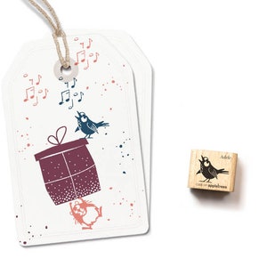 Könnte beinhalten: Ein weißes Geschenkanhänger mit einer braunen Schnur und einer rot-weißen Geschenkbox mit einem blauen Vogel, der oben drauf singt. Das Etikett hat auch rosa und blaue Noten und rosa Punkte. Das Bild ist für einen Stempel mit einem blauen Vogel, der auf einem Ast singt, mit dem Text "Adele cats on appletrees".