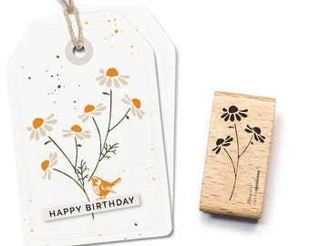 Puede incluir: Un sello de madera con un diseño en blanco y negro de una flor con un pájaro posado en una rama. El sello está etiquetado "Planted with love, Camomile & Happiness".