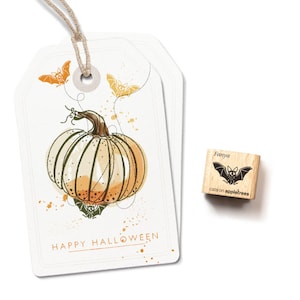Può includere: Un'etichetta regalo bianca con un'illustrazione ad acquerello di una zucca e pipistrelli. Il testo "HAPPY HALLOWEEN" è stampato sull'etichetta. È mostrato anche un piccolo timbro di legno con un disegno di pipistrello e il testo "Fanya cats on appletrees".