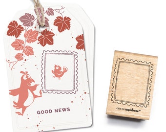 Pode incluir: Um cartão branco com um pássaro vermelho e as palavras "GOOD NEWS" impressas nele. O cartão é decorado com folhas vermelhas e um barbante marrom. Também é mostrado um carimbo de madeira com uma borda decorativa.