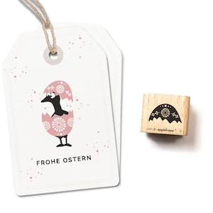 Könnte beinhalten: Ein Holz-Stempel mit einem schwarz-weißen Design eines Vogels, der aus einem Ei schlüpft. Der Stempel ist mit "cats on appletrees* 5" beschriftet. Der Text "FROHE OSTERN" ist auf einem rosa-weißen Etikett gedruckt.