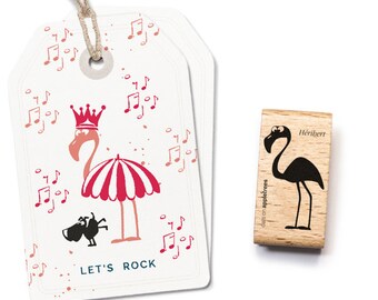 Puede incluir: Dos etiquetas de regalo blancas con una ilustración de flamenco con corona y sombrilla a rayas rojas y blancas. Las etiquetas tienen notas musicales y el texto "LET'S ROCK". También se muestra un sello de madera con una silueta de flamenco negro.