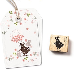 Könnte beinhalten: Zwei weiße Geschenkanhänger mit einer Schnur, mit einer skurrilen Illustration eines Vogels, der einen Blumen-Regenschirm hält, mit den Worten "BE HAPPY". Ein Holzstempel mit passendem Vogeldesign ist ebenfalls vorhanden.