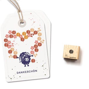 May include: Two white gift tags with a floral heart design and a cartoon sheep. The tags have a string for hanging. A small wooden stamp with a flower and the text "69 catson appletrees" is also present.