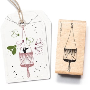 May include: A wooden rubber stamp featuring a hanging planter design. The stamp is made by Cats on Appletrees and depicts a simple black line drawing of a hanging planter with a tassel.