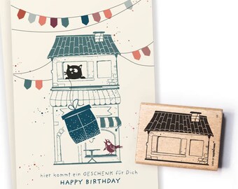 Puede incluir: Una tarjeta de cumpleaños con un gato negro asomándose por la ventana de una casa con una caja de regalo colgando de una cuerda. La tarjeta tiene el texto "hier kommt ein GESCHENK für Dich HAPPY BIRTHDAY".