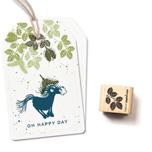 May include: A white card with a green and blue illustration of a horse with a leafy crown. The text "OH HAPPY DAY" is printed below the horse. A small wooden stamp with a black illustration of leaves is also shown. The stamp is labelled "cats on appletrees".