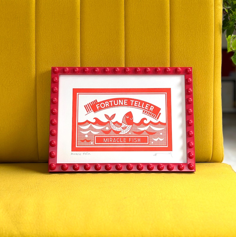 May include: A red framed print with a white illustration of a fish with the text "Fortune Teller Miracle Fish" inside a red and white box.