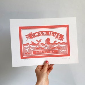 May include: A red and white print of a fortune teller box with the text "FORTUNE TELLER" and "MIRACLE FISH". The box features a cartoon fish with a happy face.