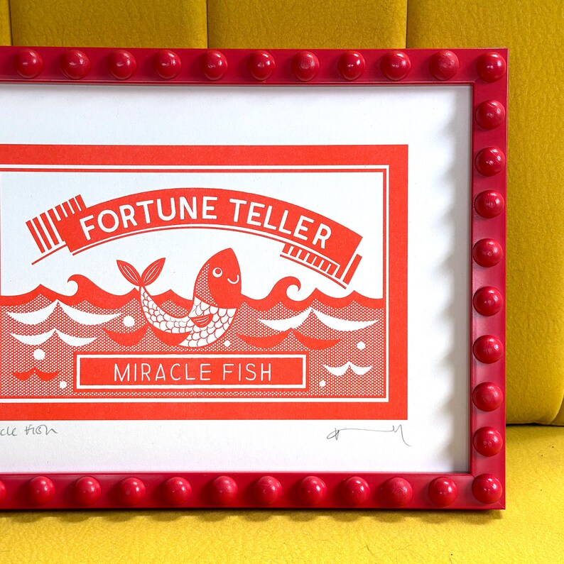 May include: A red framed print with a white background and a red illustration of a fish with the text "Fortune Teller Miracle Fish" in white.