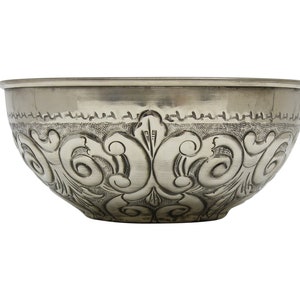 May include: A silver-coloured bowl featuring an embossed floral design. The bowl has a wide, shallow shape with a slightly flared rim. The detailed pattern includes scrolling leaves and symmetrical elements, creating a vintage aesthetic.