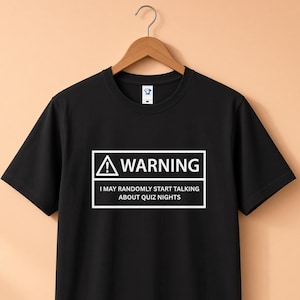 May include: A black short-sleeved t-shirt featuring a white rectangular graphic with a warning triangle icon and the text: WARNING I MAY RANDOMLY START TALKING ABOUT QUIZ NIGHTS. The shirt is displayed on a wooden hanger against a solid light-coloured background.
